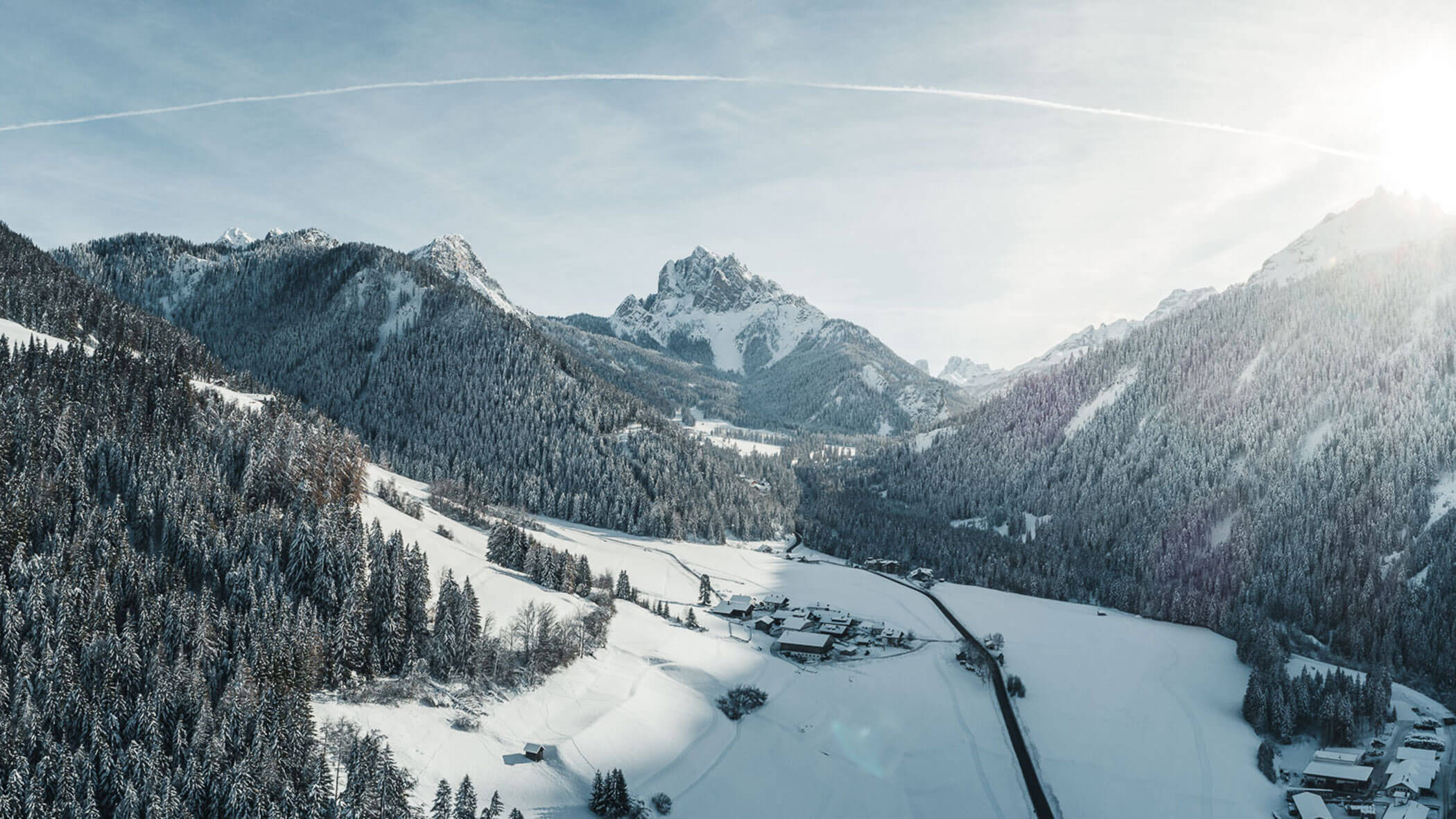 Das Dorf Prags von oben im Winter mit schneebedeckten Bäumen und Bergen - Kuenzerhof